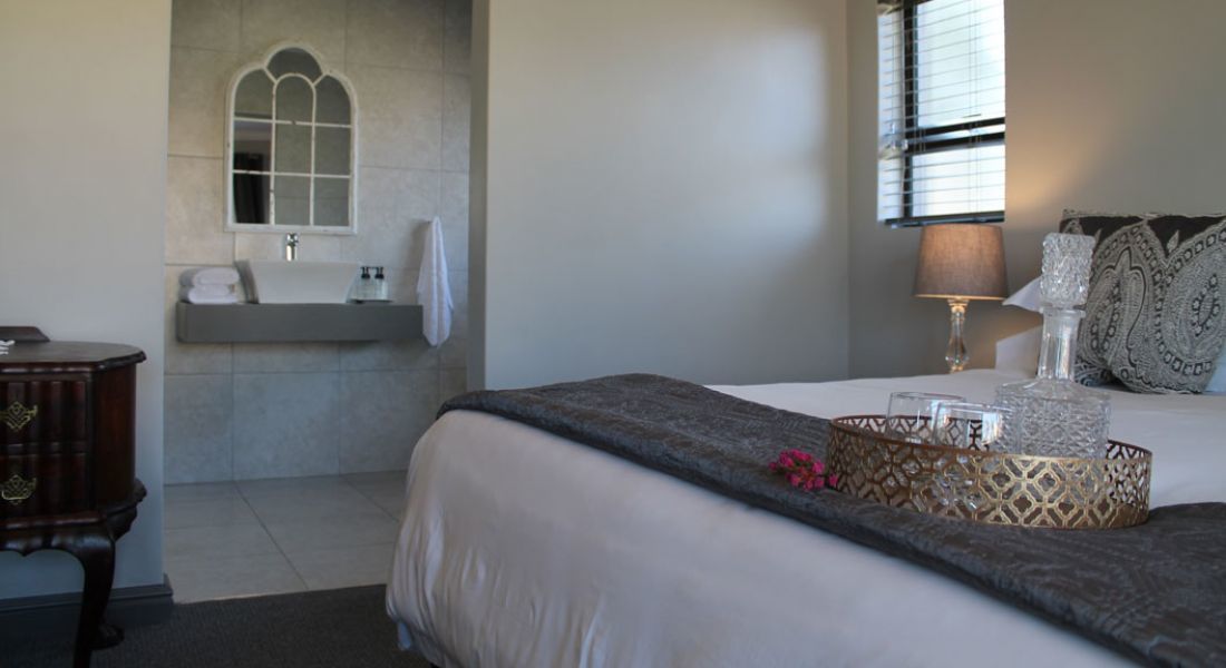 A bedroom with a bed, bedside table, lamp, decorative pillows, and a window with blinds.