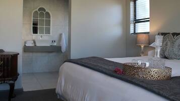 A bedroom with a bed, bedside table, lamp, decorative pillows, and a window with blinds.