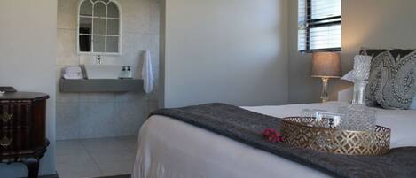 A bedroom with a bed, bedside table, lamp, decorative pillows, and a window with blinds.