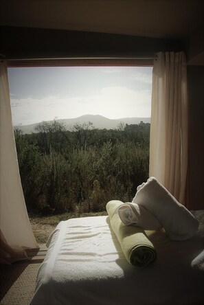 A hotel room with a bed, a rolled-up towel, and a view of a natural landscape through a window. - Forest Nature Spa (The Crags)
