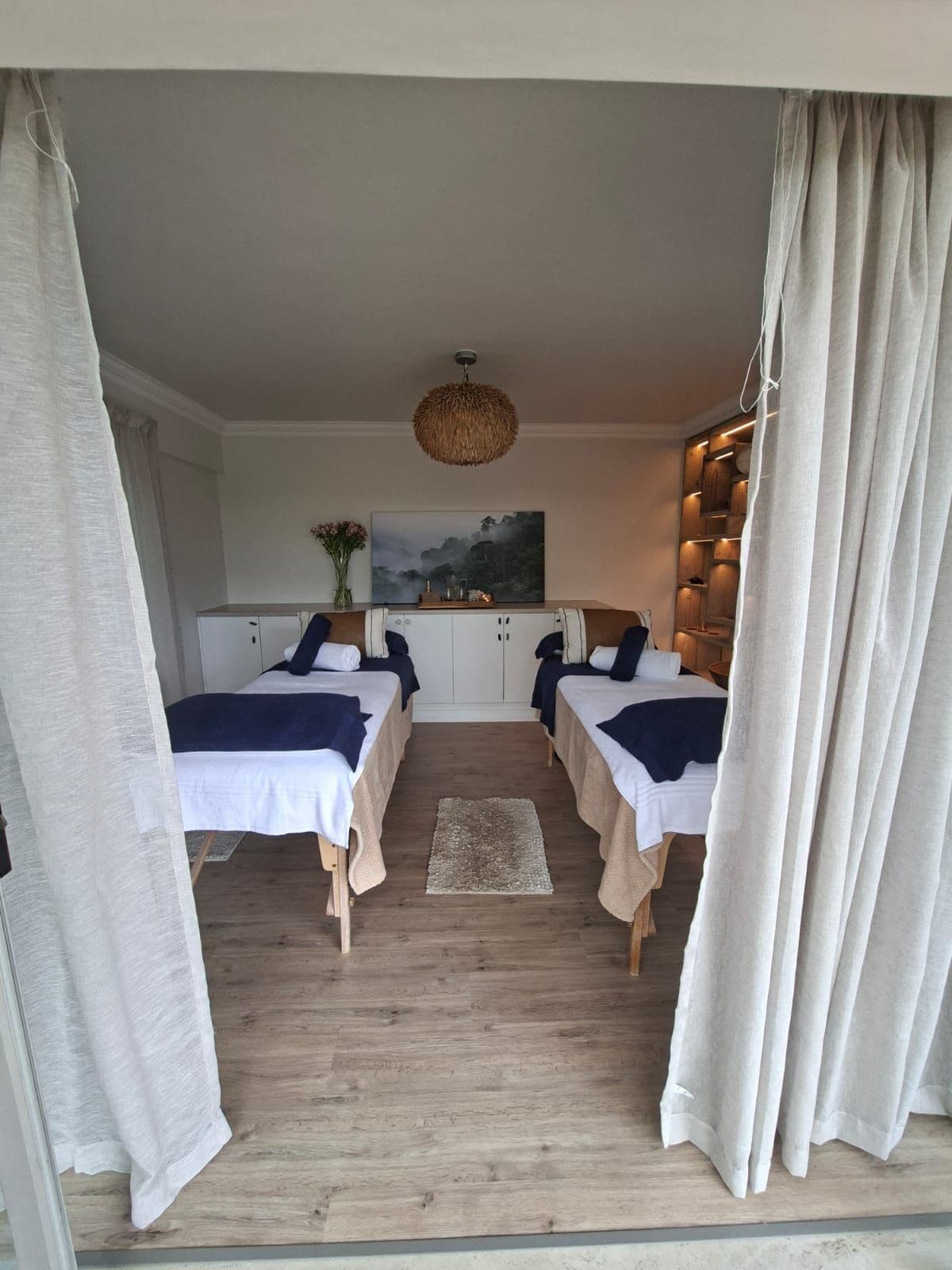 Une chambre avec deux lits, un plancher en bois, un luminaire suspendu et un tableau au mur.