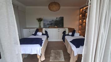 A room with two beds, a wooden floor, a hanging light fixture, and a painting on the wall.