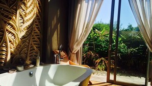Ein modernes Badezimmer mit freistehender Badewanne, einer dekorativen Wandverkleidung und Blick auf üppiges Grün durch große Schiebeglastüren.