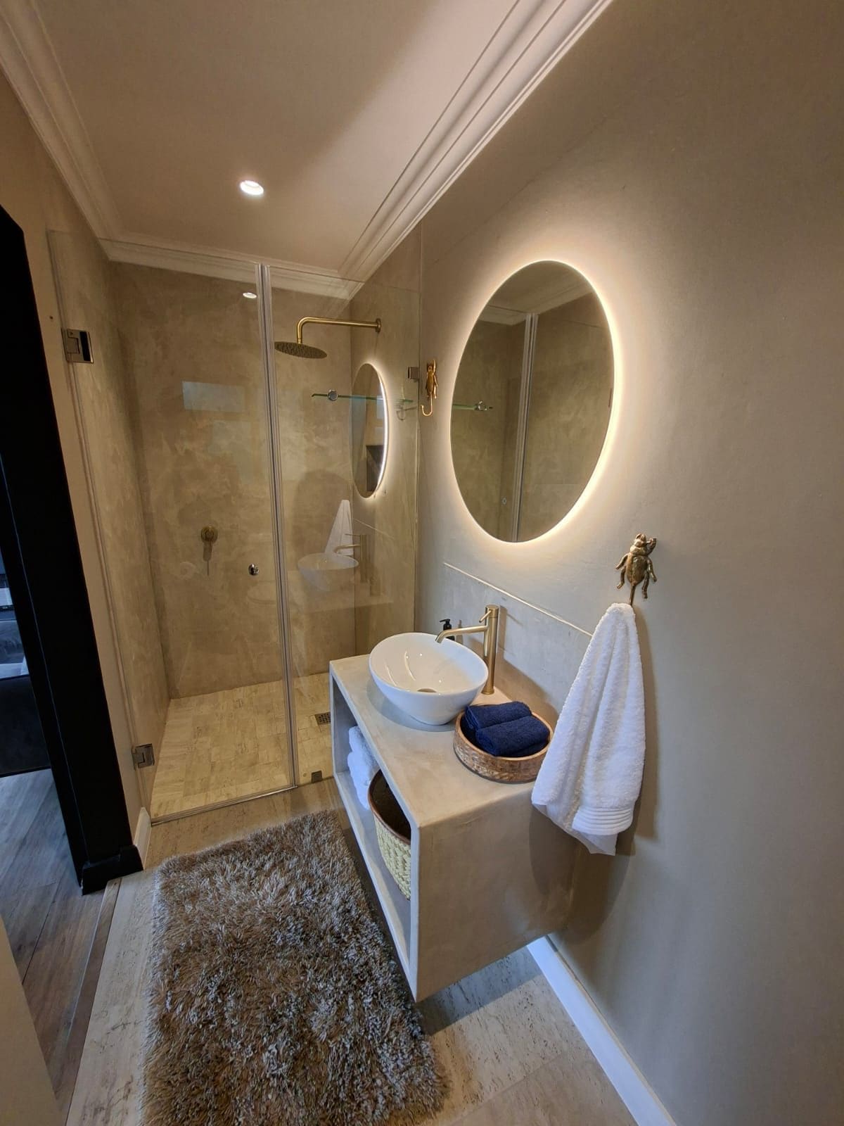 A modern bathroom with a glass-enclosed shower, a round mirror, a white sink, and a towel rack.
