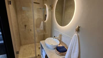 A modern bathroom with a glass-enclosed shower, a round mirror, a white sink, and a towel rack.