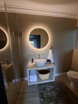 A modern bathroom with a round mirror, a vessel sink, and a toilet. - Forest Nature Spa (Plettenberg Bay)