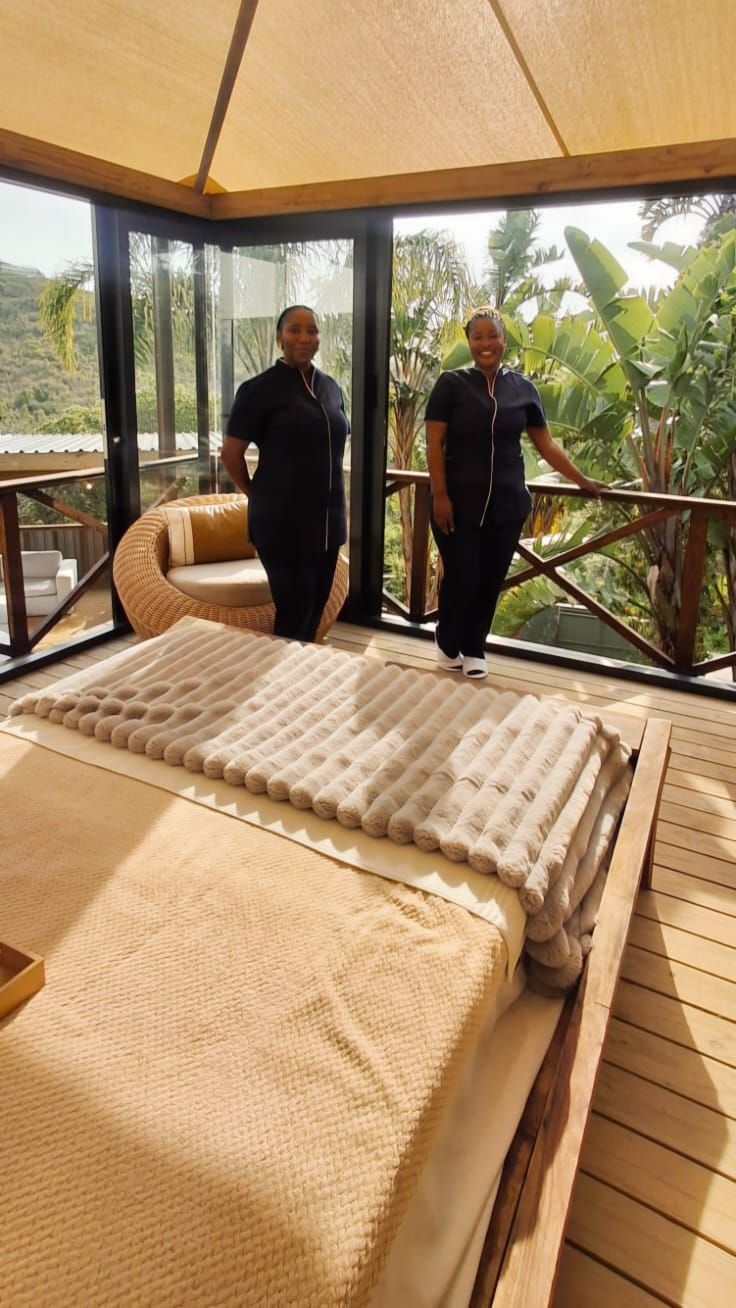 Una habitación con una cama grande, suelo de madera, pared de vidrio y vista a zonas verdes.