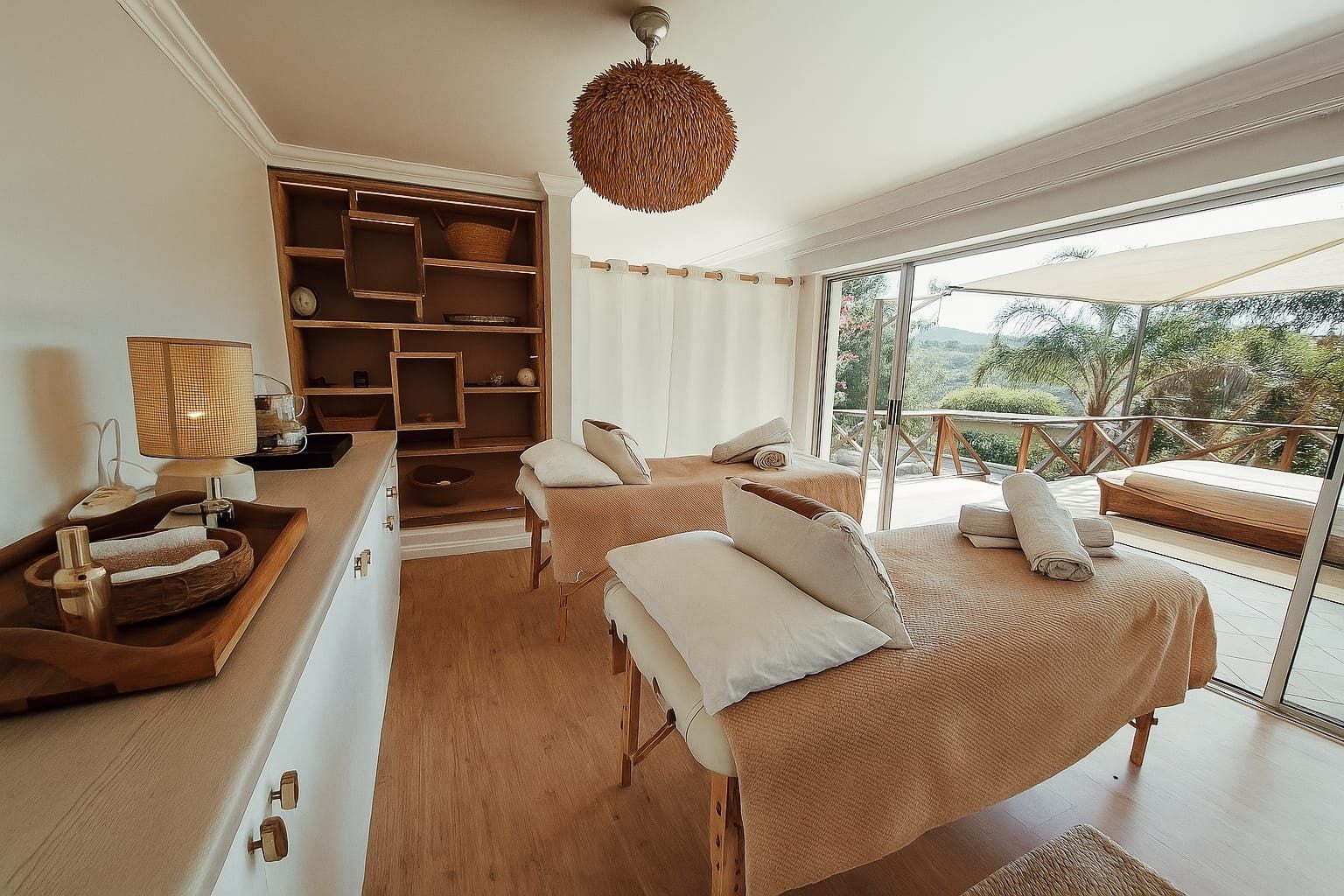 A bedroom with a large bed, a bedside table, a lamp, a shelf with baskets, and a view of the outdoors.
