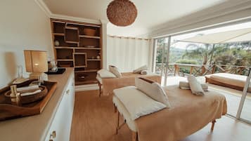 A bedroom with a large bed, a bedside table, a lamp, a shelf with baskets, and a view of the outdoors.