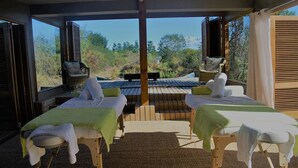 Ein Wellnessbereich mit zwei Massagetischen, einer Sitzbank und Blick auf die umliegende Landschaft.