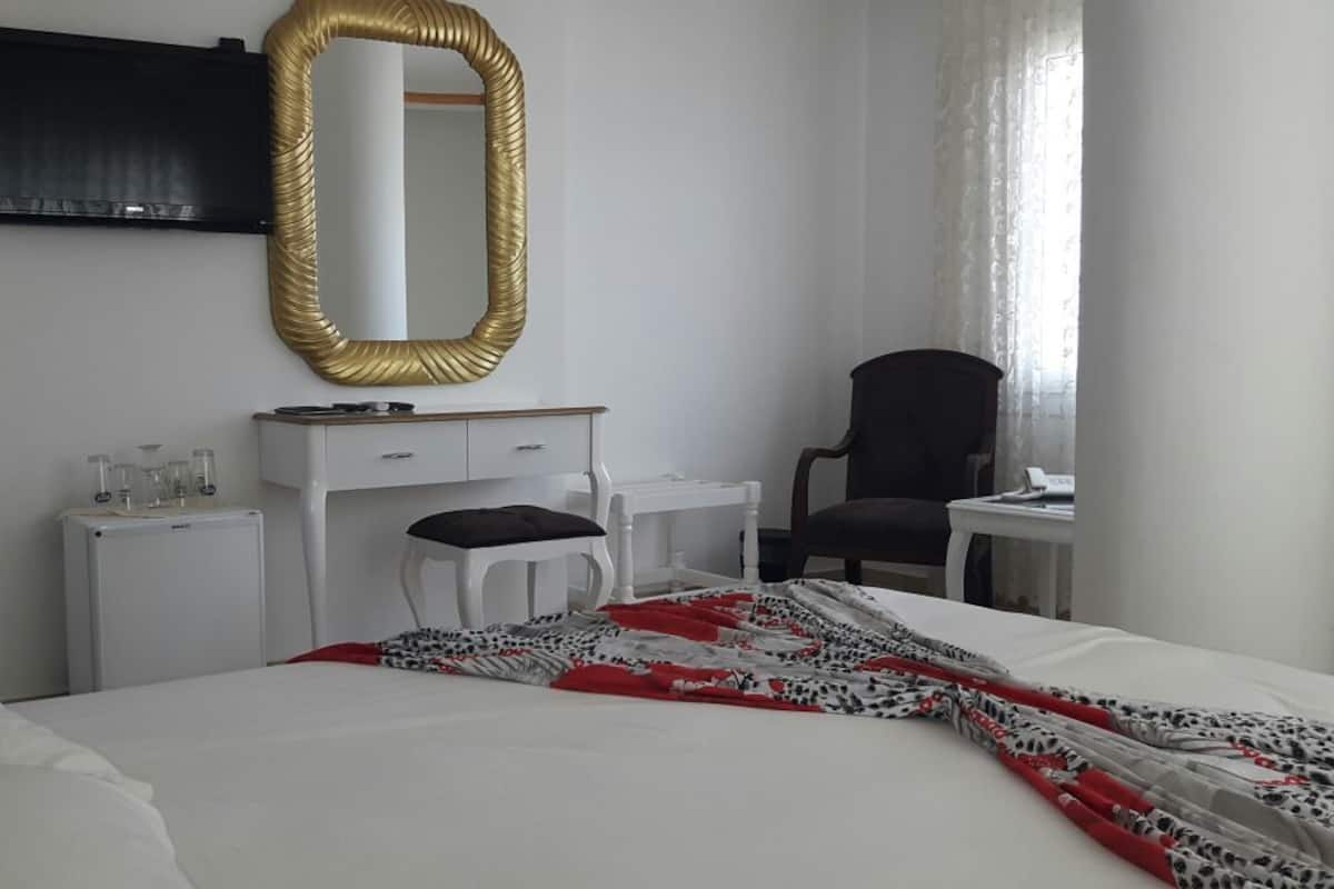 Habitación de hotel con cama, escritorio, silla, televisor y ventana con cortinas.