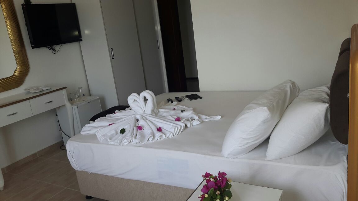A hotel room with a bed, a desk with a mirror, a flat-screen TV, and a small table with a vase of flowers.