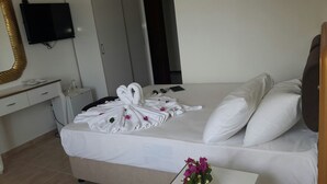 A hotel room with a bed, a desk with a mirror, a flat-screen TV, and a small table with a vase of flowers. - Jasmin Blue Otel (Silifke)