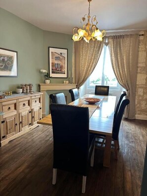 Un espace repas comprenant une table en bois, des chaises, un lustre et une vue sur l’extérieur.