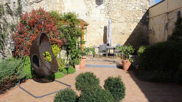 Une cour avec un mur en pierre, une chaise suspendue, des plantes en pot et une table avec des chaises.