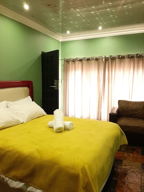 A room with a bed, a brown sofa, a window with curtains, and a door. - Lake Sands Manor (Pietermaritzburg)