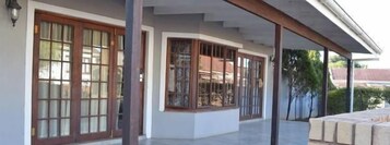 Un porche cubierto con suelo de baldosas, amplias ventanas de madera y vistas a una zona residencial.