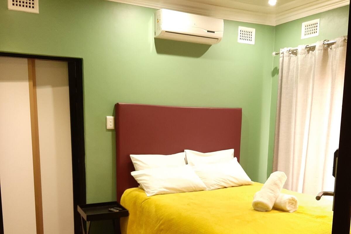 Een hotelkamer met een bed, nachtkastje, airconditioning en een badkamer met gordijn.