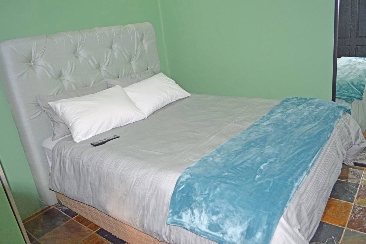 Een bed met een gestoffeerd hoofdbord, twee kussens en een blauwe deken.