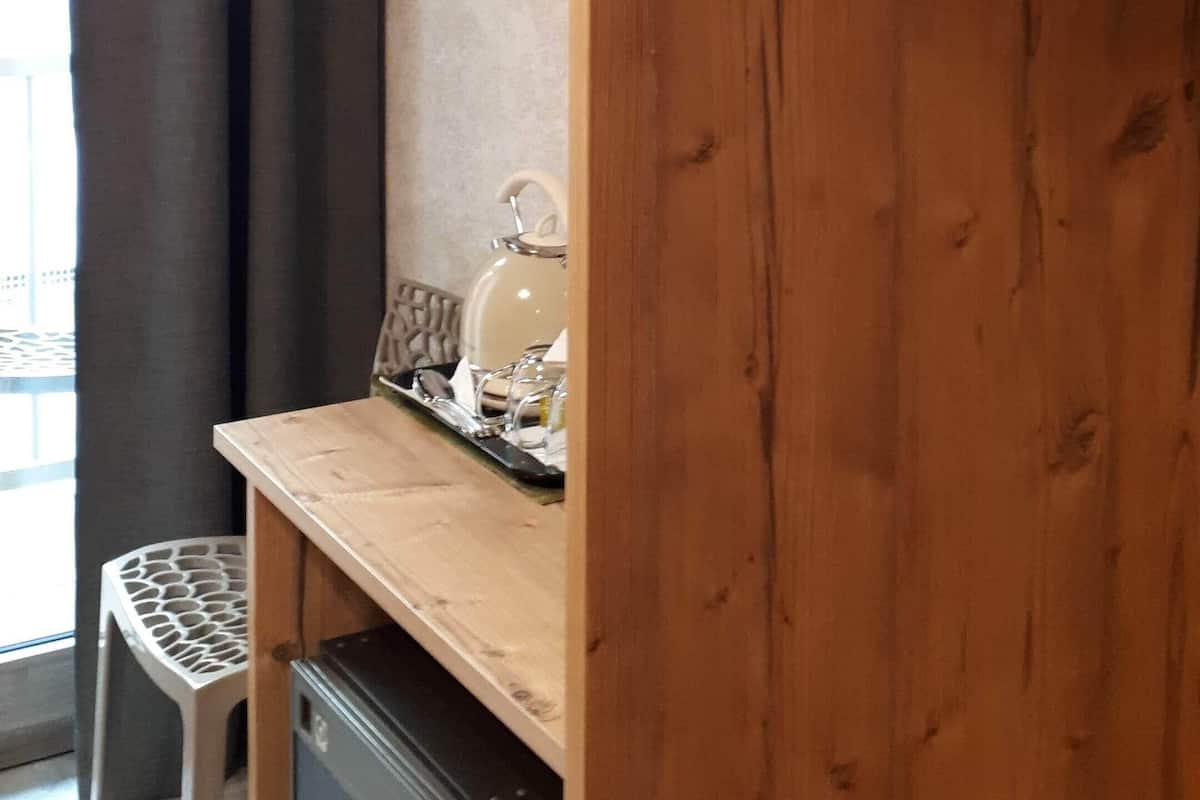 A wooden wardrobe with a hanging rack, a small table with a kettle, and a chair.