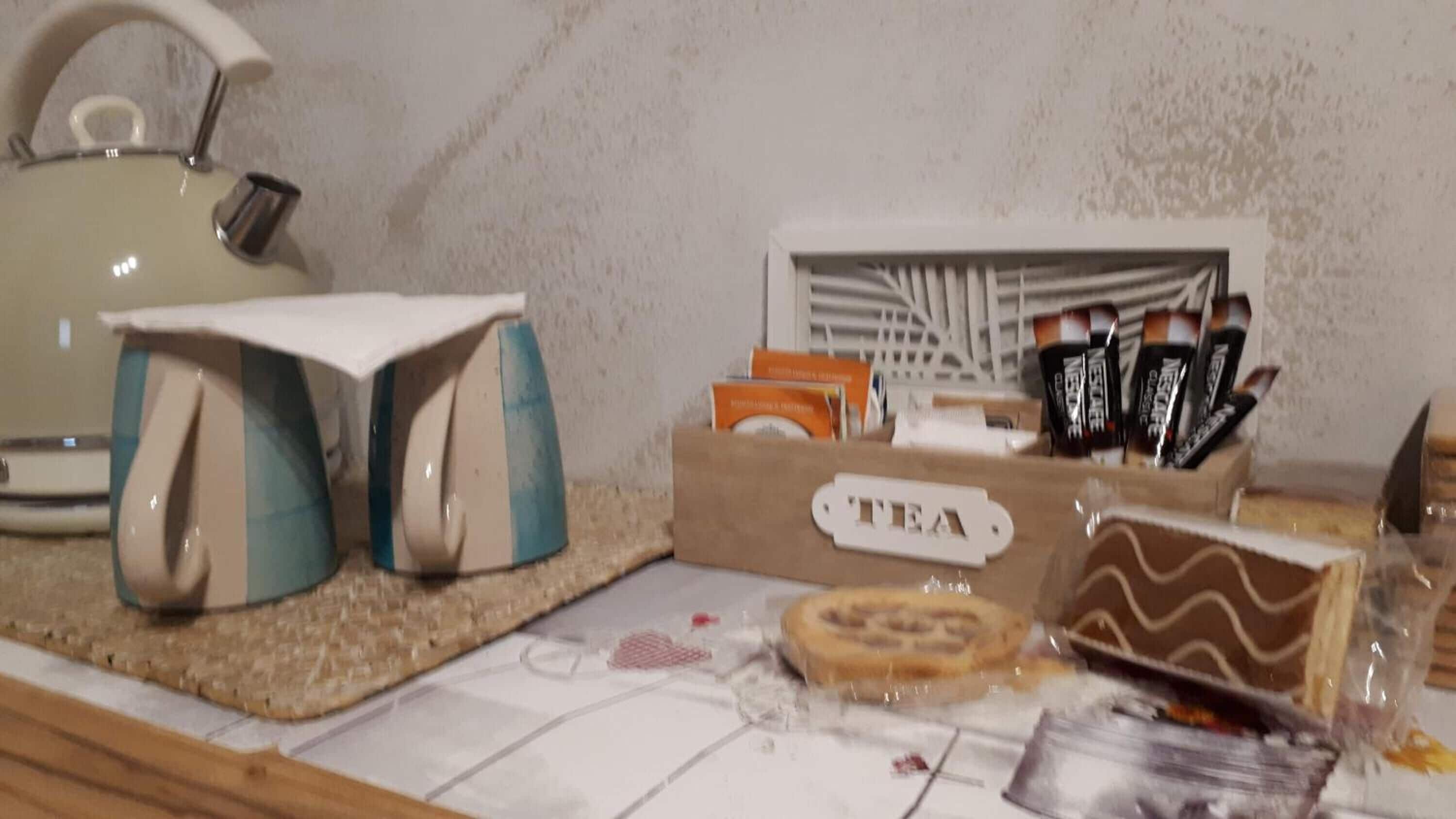 A kitchen counter with a kettle, teapots, a box labeled "TEA", and some packaged tea bags.