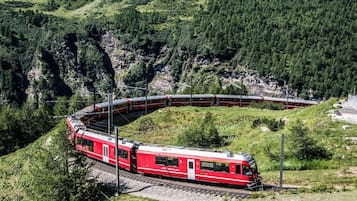 A red train on a curved track through a mountainous area.