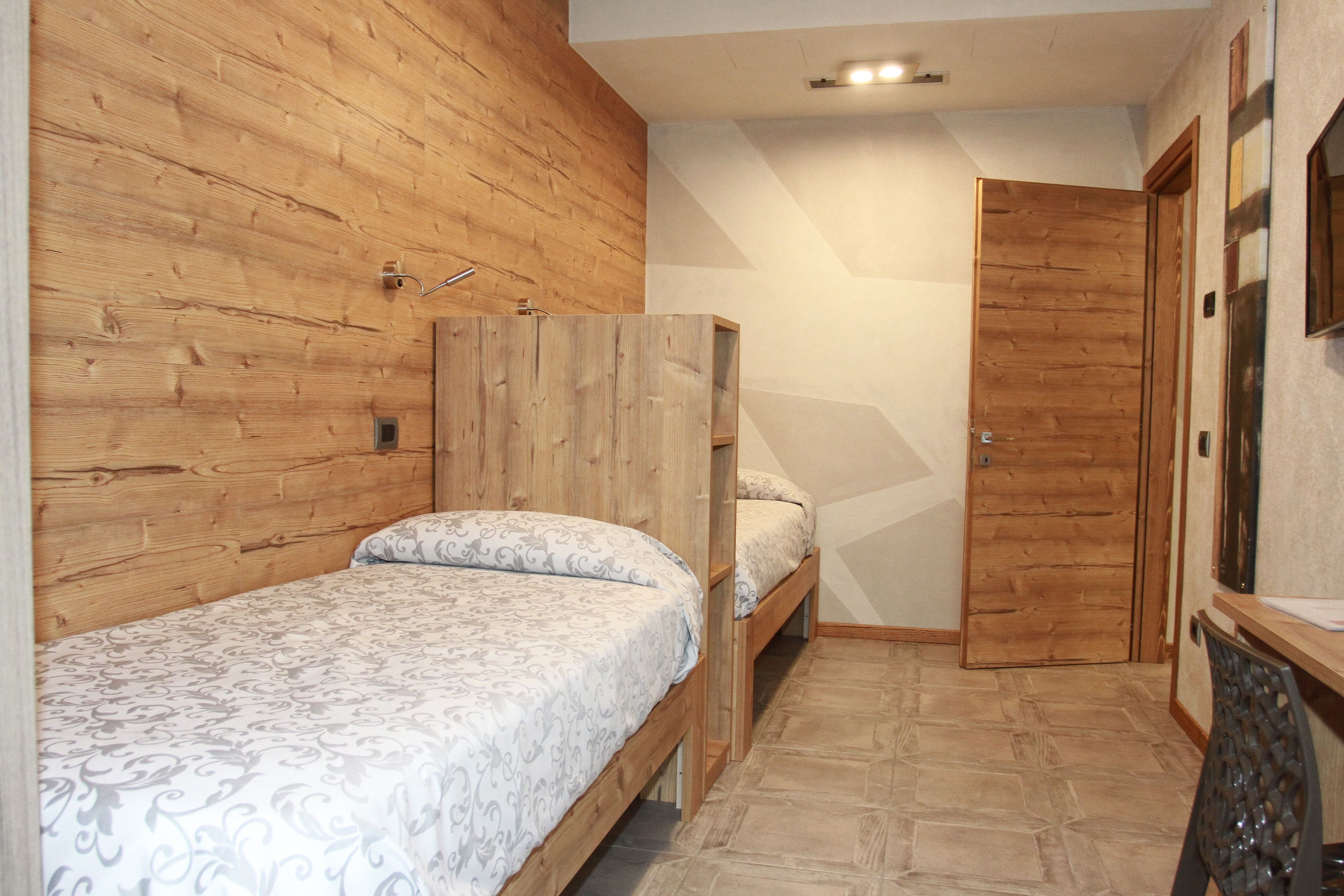 Une chambre avec deux lits superposés en bois, une armoire en bois et un sol carrelé.