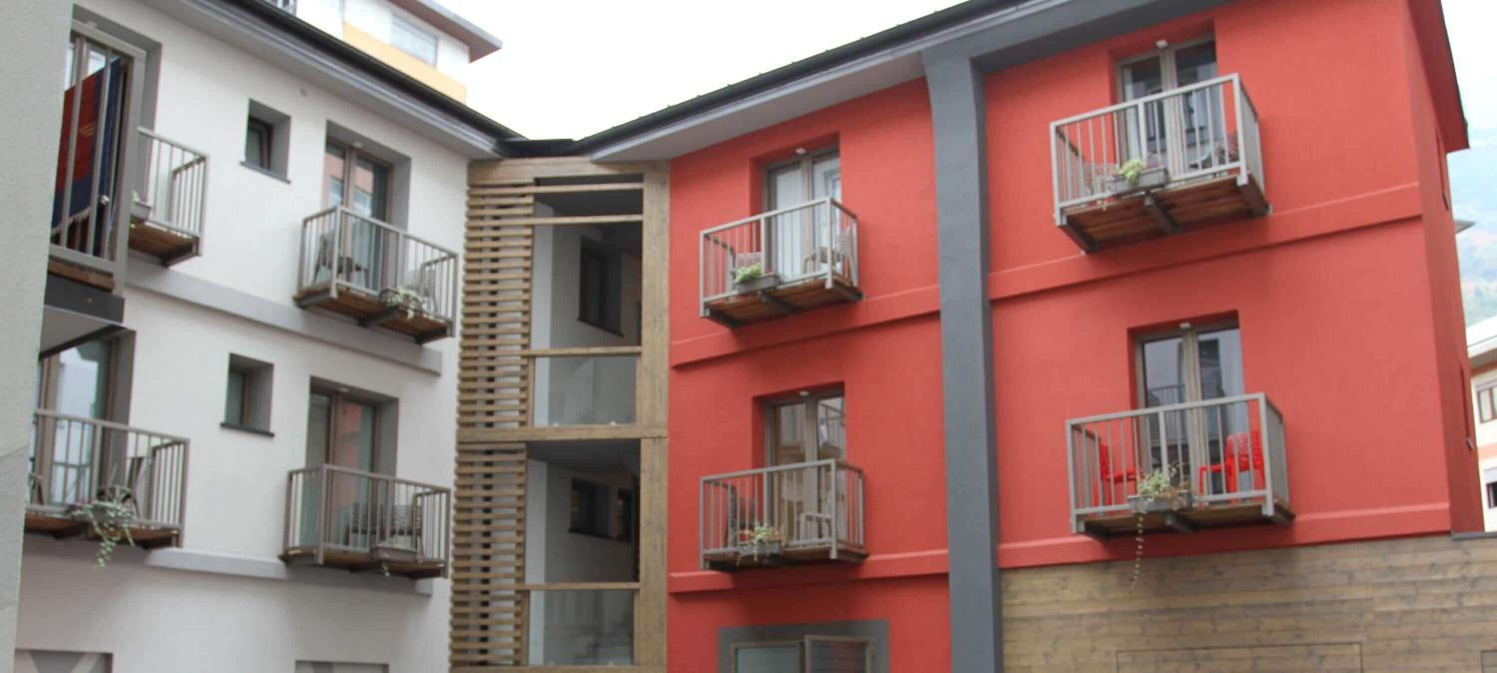 Un immeuble à plusieurs étages doté de balcons, d’un mur à lamelles de bois et d’une façade rouge.