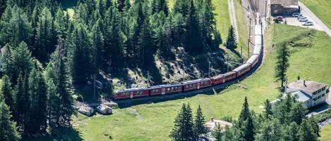 Un tren serpentea por una zona boscosa con un edificio pequeño y una carretera cerca.