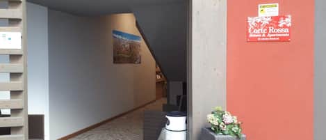 A hallway with a staircase, a poster on the wall, and a sign for Corte Rossa Rooms & Apartments.