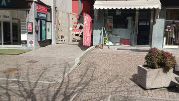 A cobblestone plaza with a café, a check-in kiosk, and a building with a balcony.