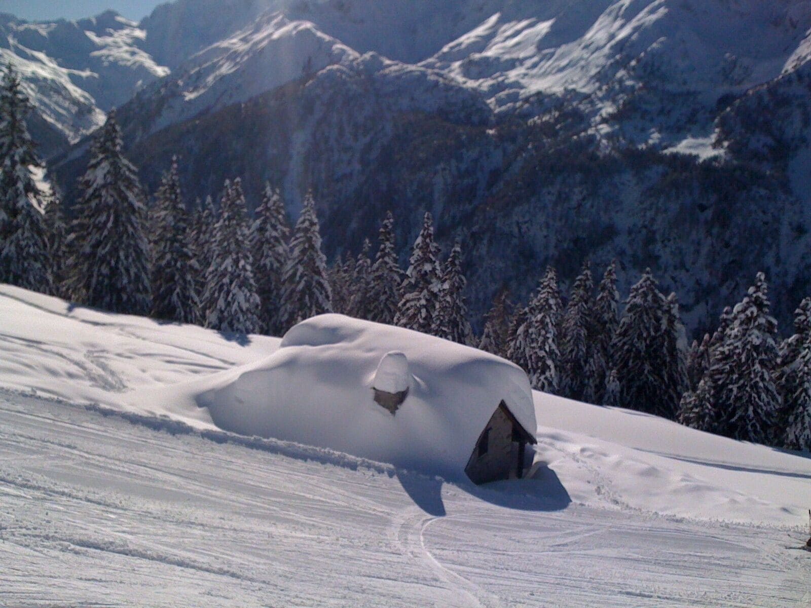 A snow-covered mountain with a cabin partially buried in snow.