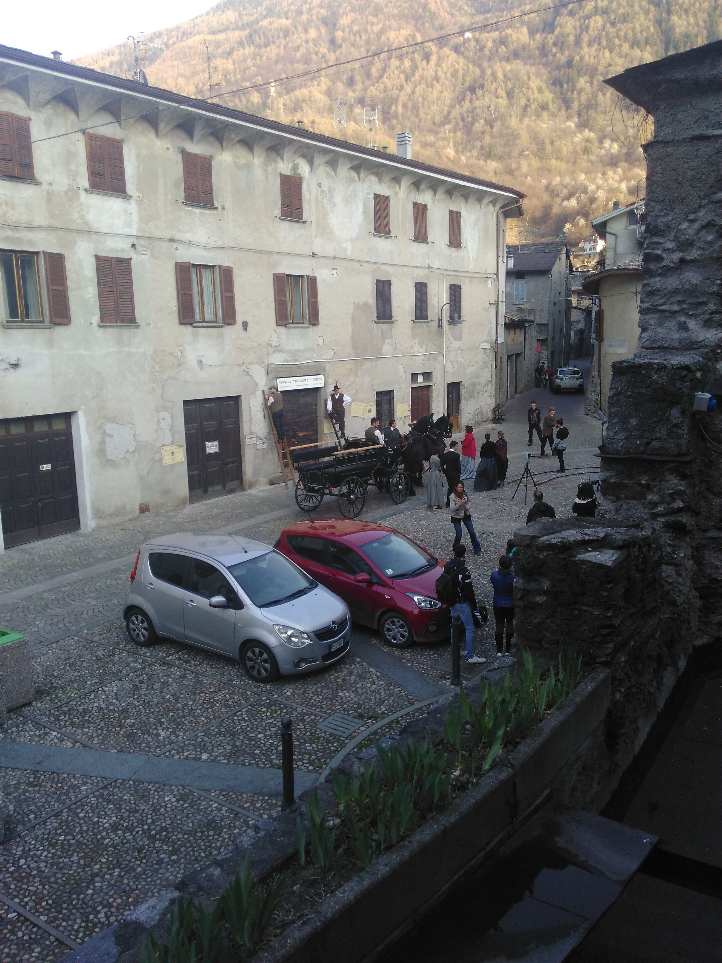 Una calle estrecha con edificios históricos, coches estacionados y un carruaje tirado por caballos.