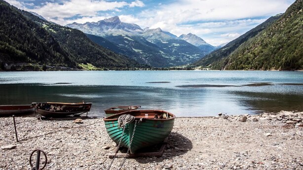 A lakeside scene with boats on a pebbly shore, surrounded by mountains and a clear sky. - B&B Corte Rossa (Tirano)