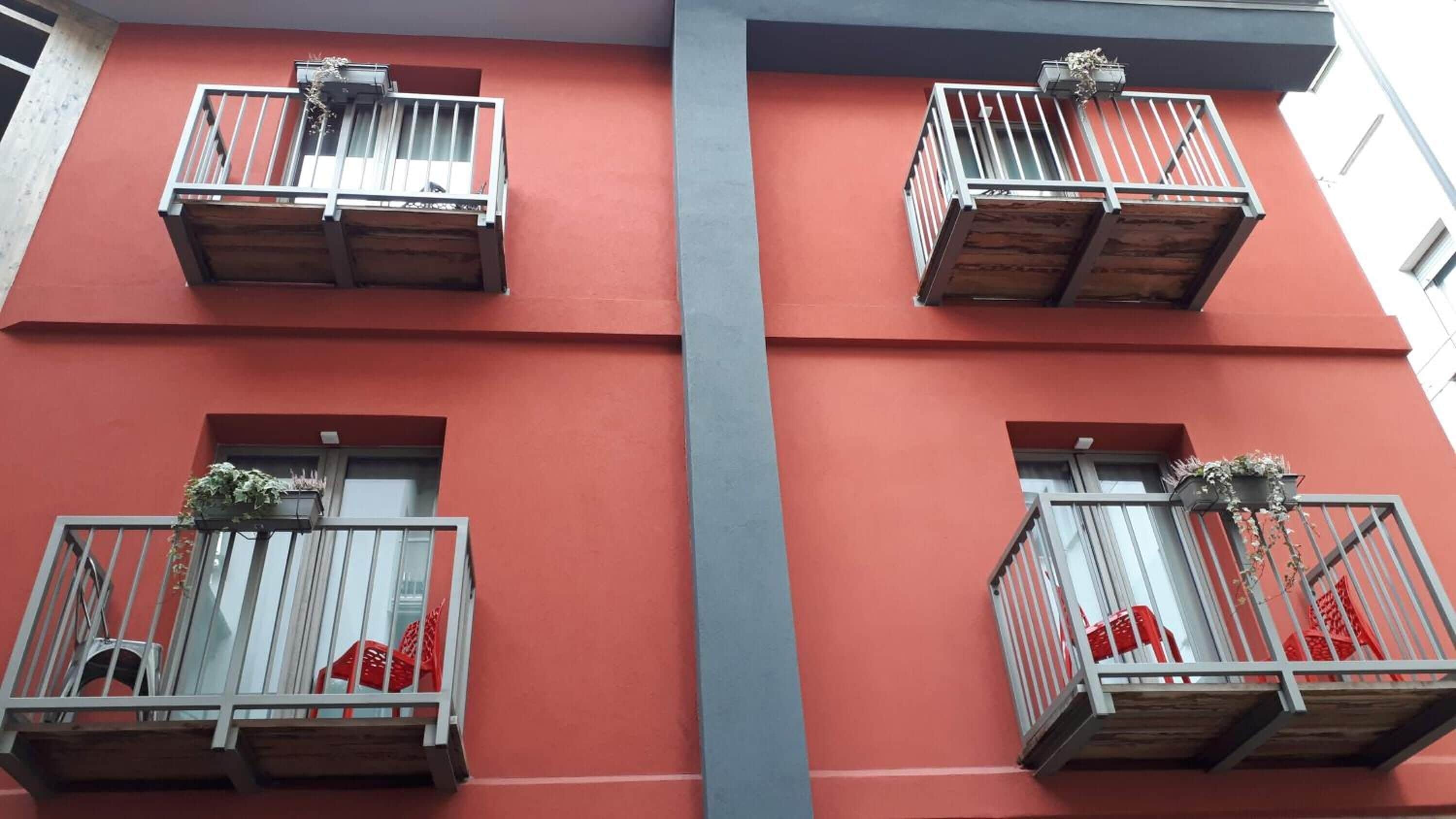 A building with red walls and balconies with metal railings and wooden platforms.