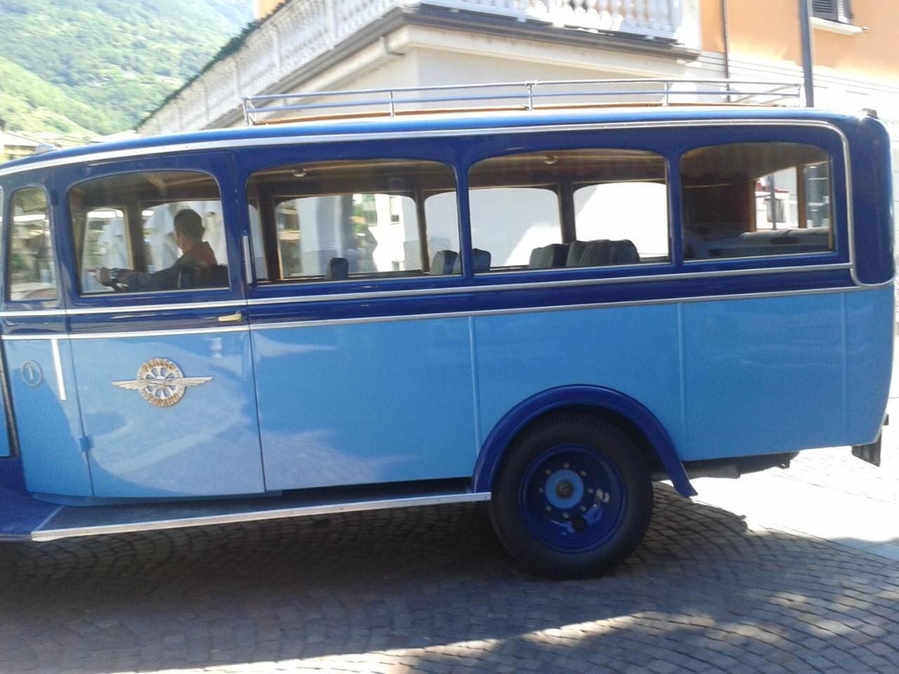 Ein blauer Vintage-Bus mit einem Logo an der Seite, geparkt in einer Kopfsteinpflasterstraße.