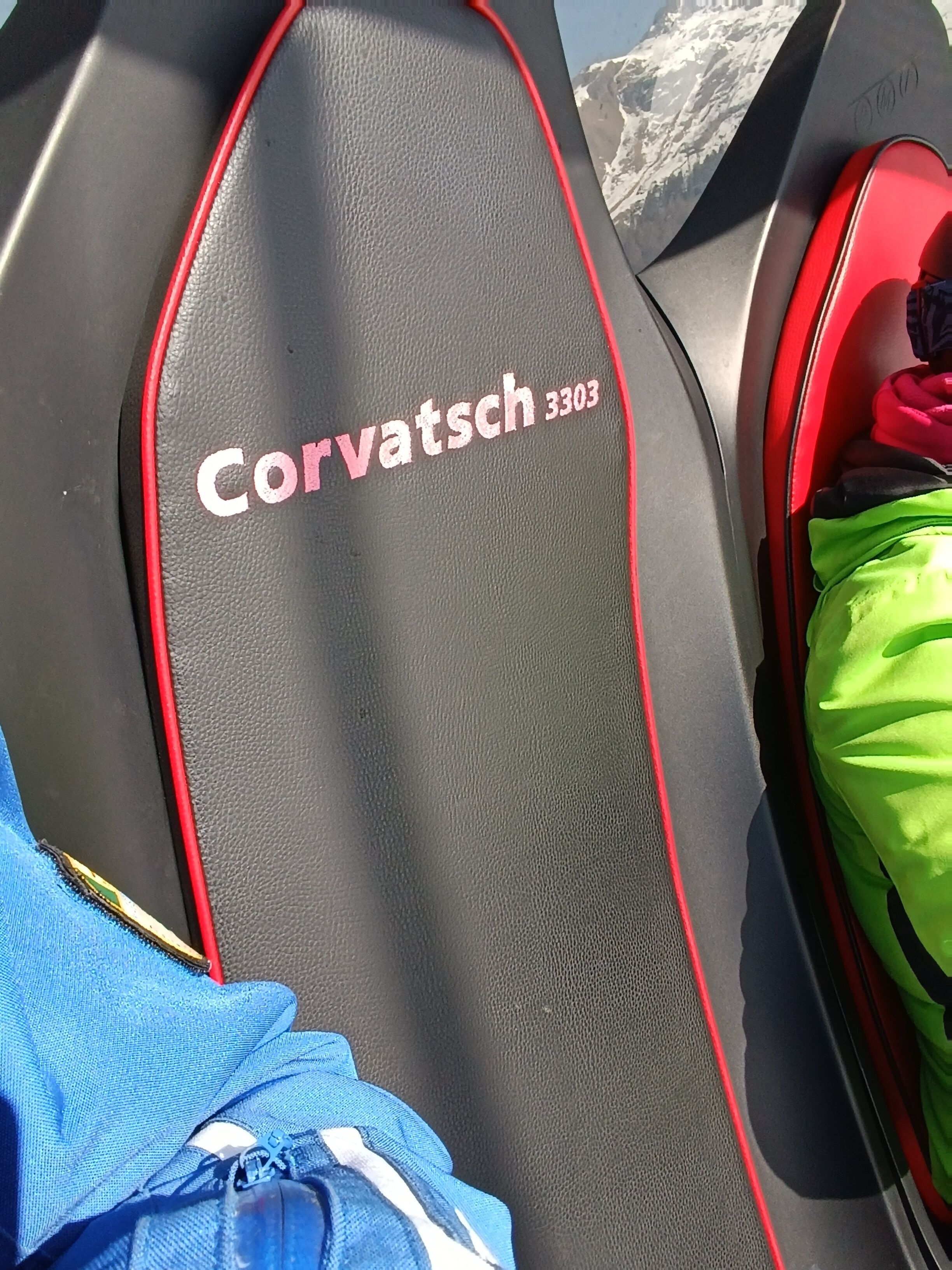 Un siège en cuir noir orné en relief du nom « Corvatsch 3303 », avec des détails de coutures rouges, et un sac vert en arrière-plan.