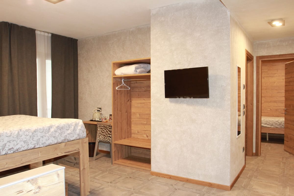 A bedroom with a bed, a desk, a TV mounted on the wall, and a wardrobe.