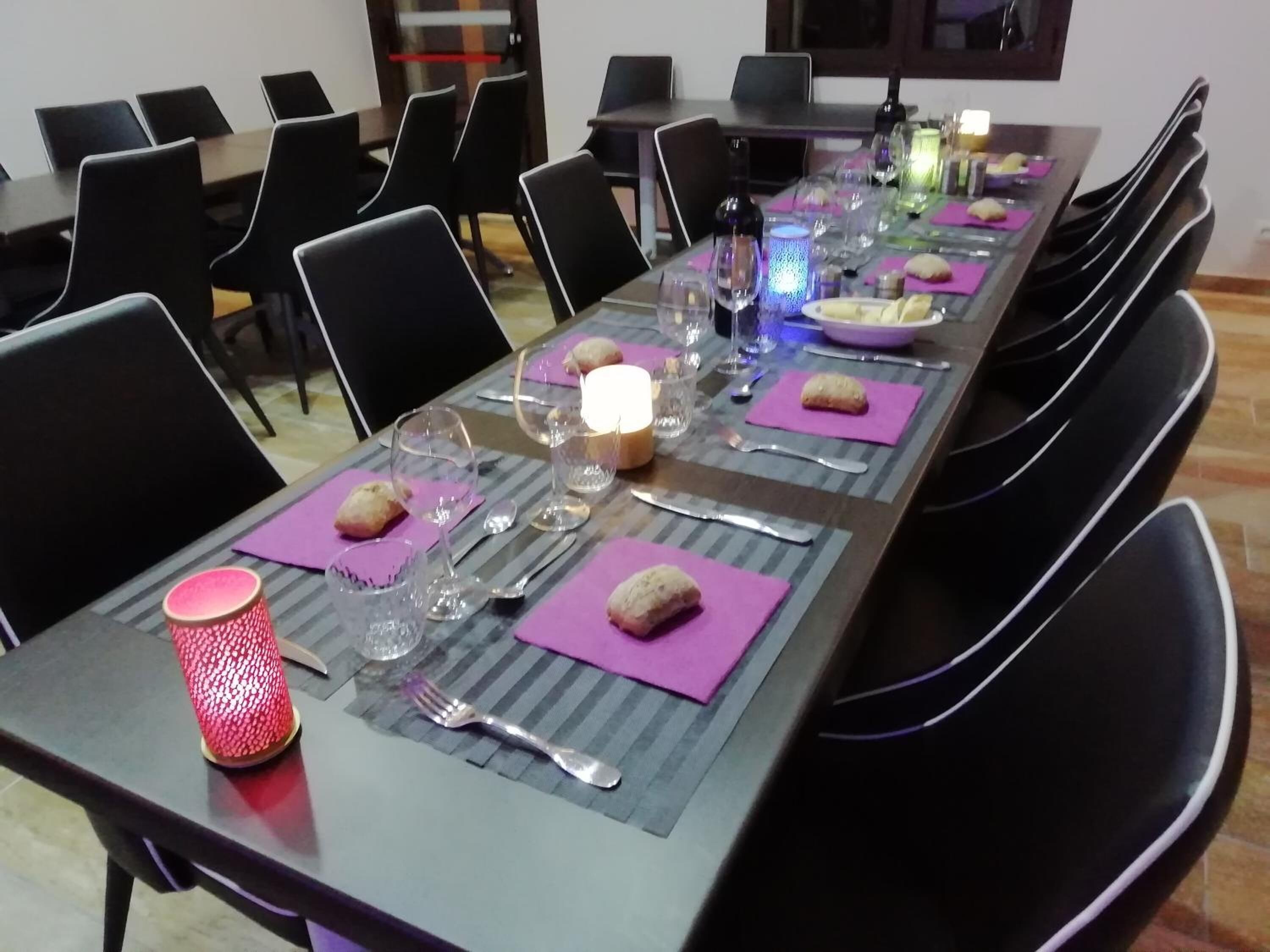 Una mesa de comedor dispuesta con platos, cubiertos y vasos, rodeada de sillas negras.