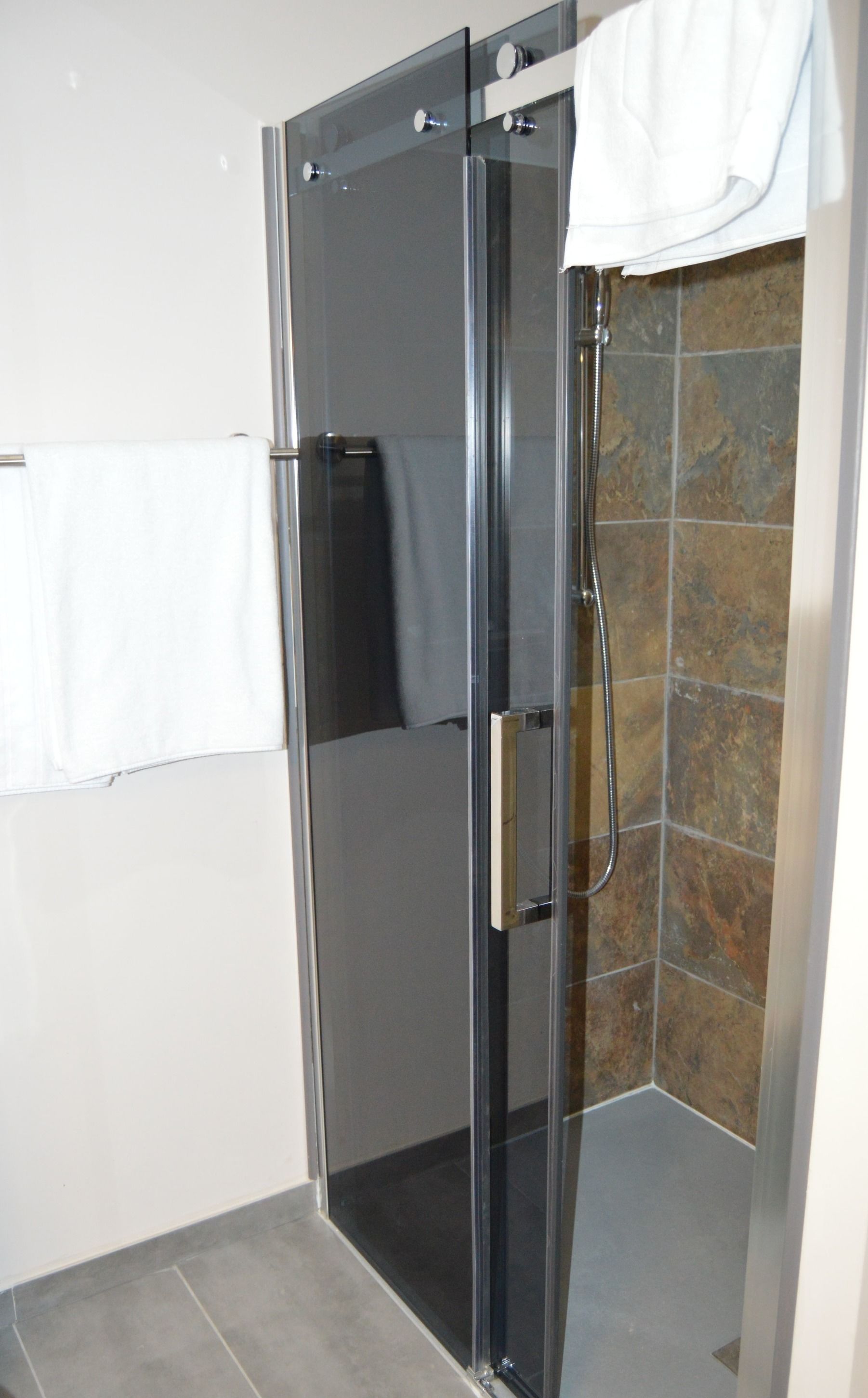 A glass-enclosed shower with a handheld showerhead, a towel rack, and a tiled wall.