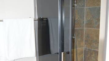 A glass-enclosed shower with a handheld showerhead, a towel rack, and a tiled wall.