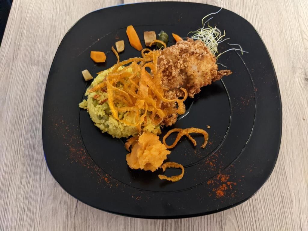 A black plate with a food dish, possibly a fried item, and some vegetables.