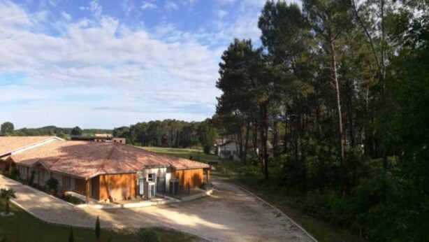 A large building with a tiled roof, surrounded by a well-maintained lawn and trees. - L'Hôtel du Lac (Casteljaloux)