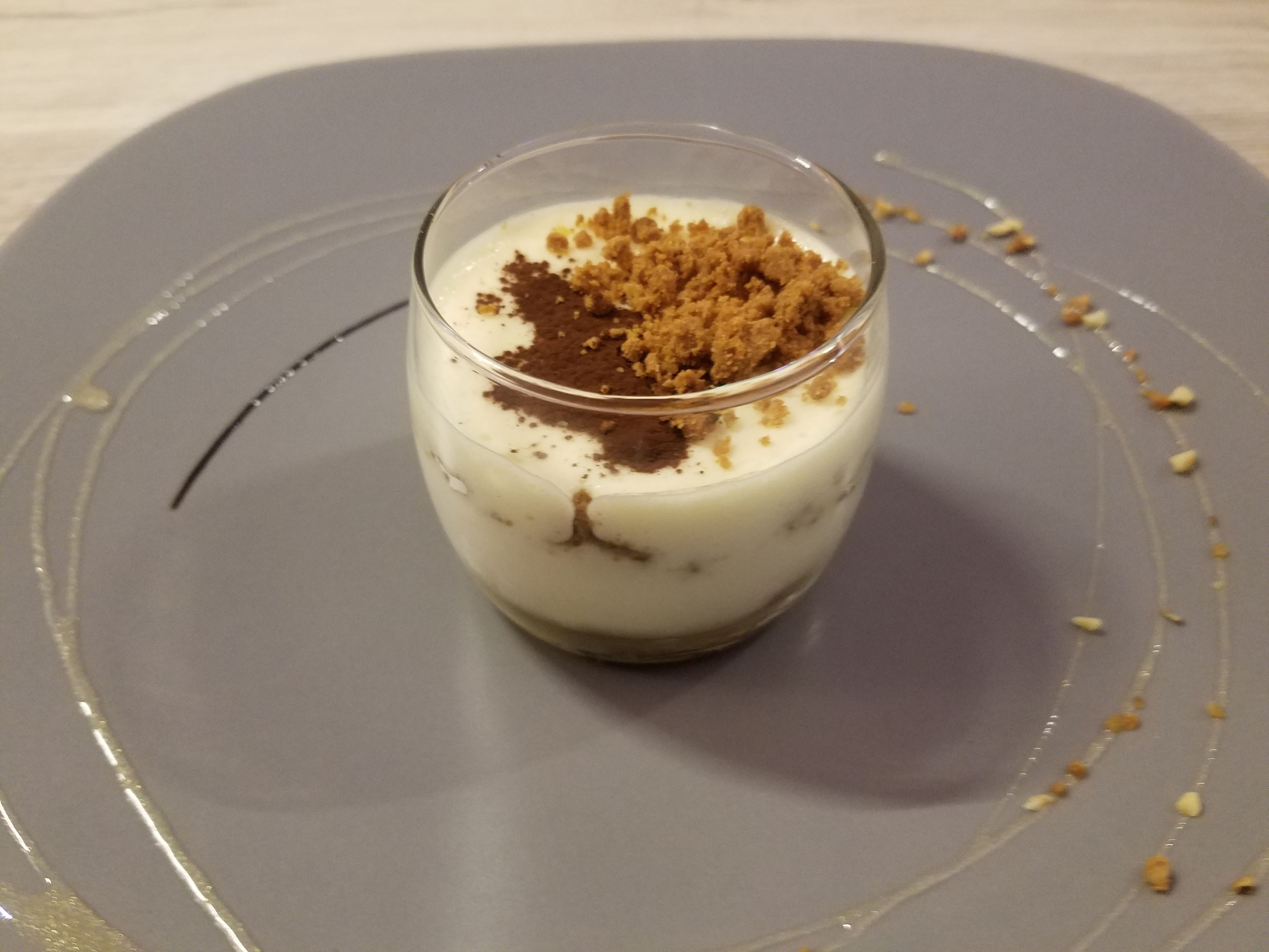 Un postre en un vaso sobre un plato con un diseño decorativo alrededor.