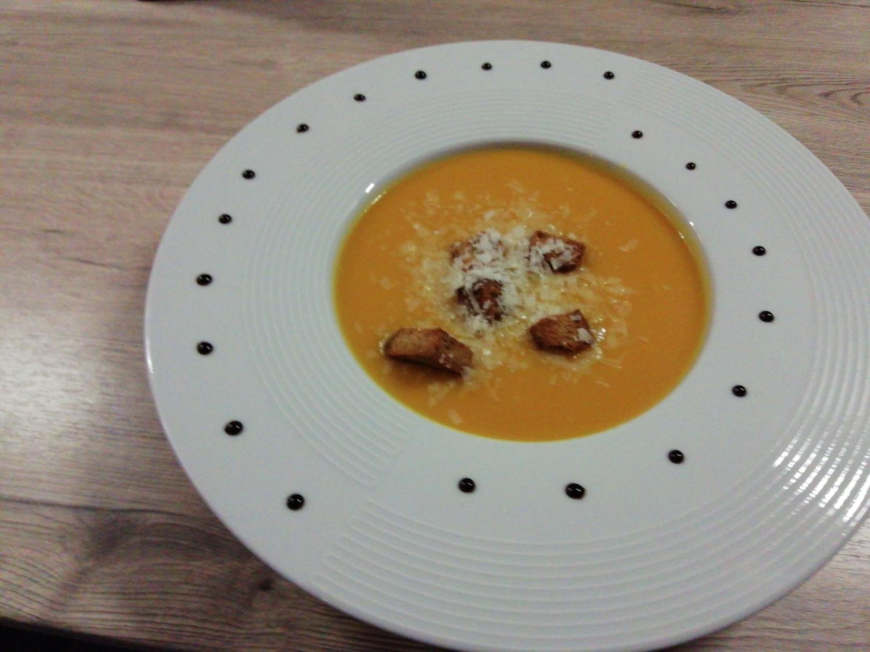 Une assiette blanche contenant une soupe et des croûtons, posée sur une table en bois.