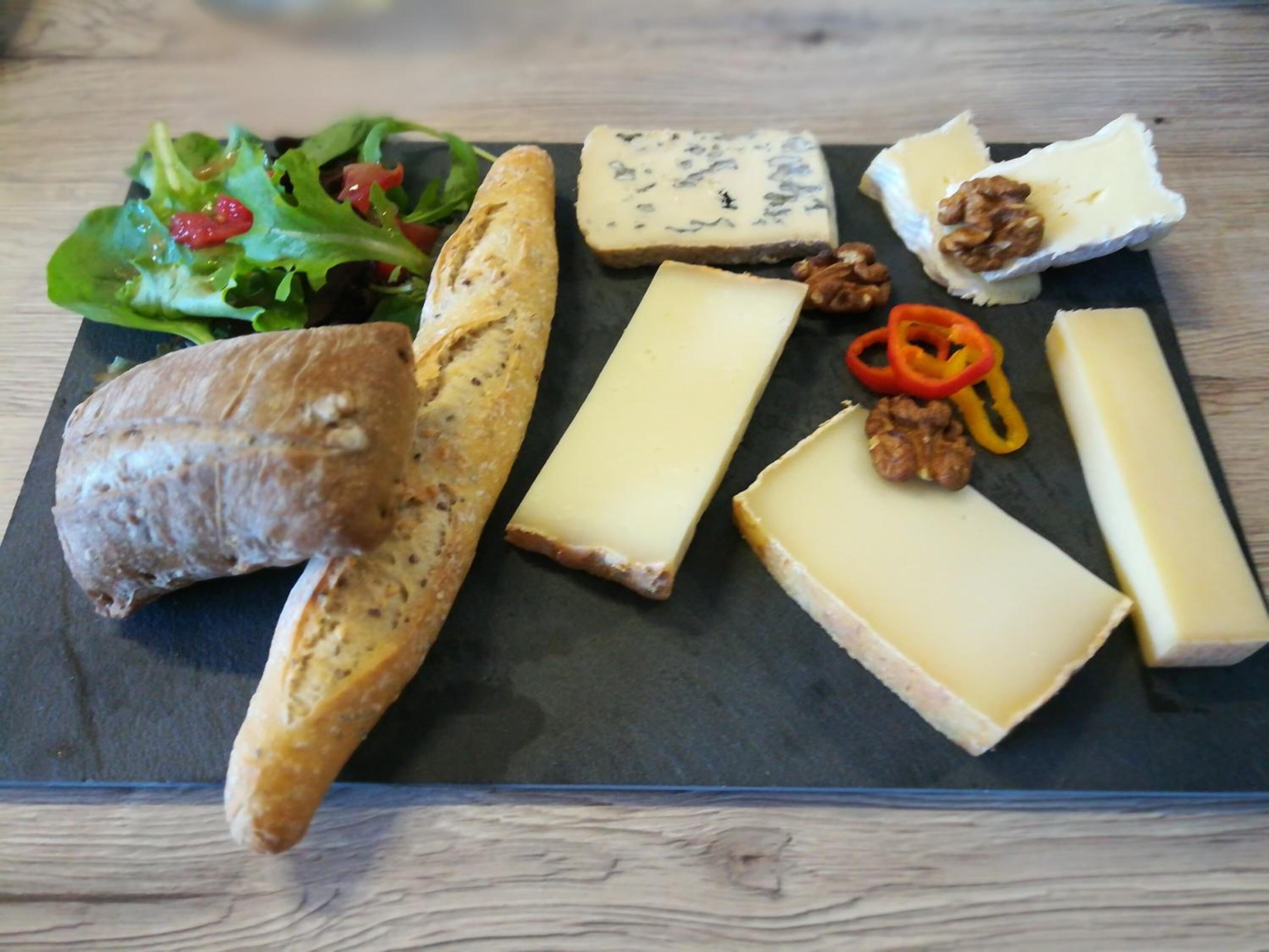 Una tabla de fiambres con varios quesos, frutos secos y pan sobre una tabla de pizarra.