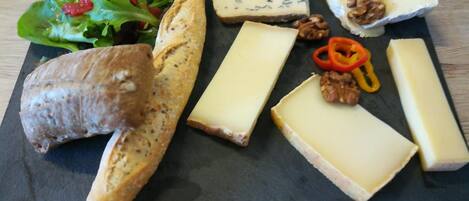 Una tabla de fiambres con varios quesos, frutos secos y pan sobre una tabla de pizarra.
