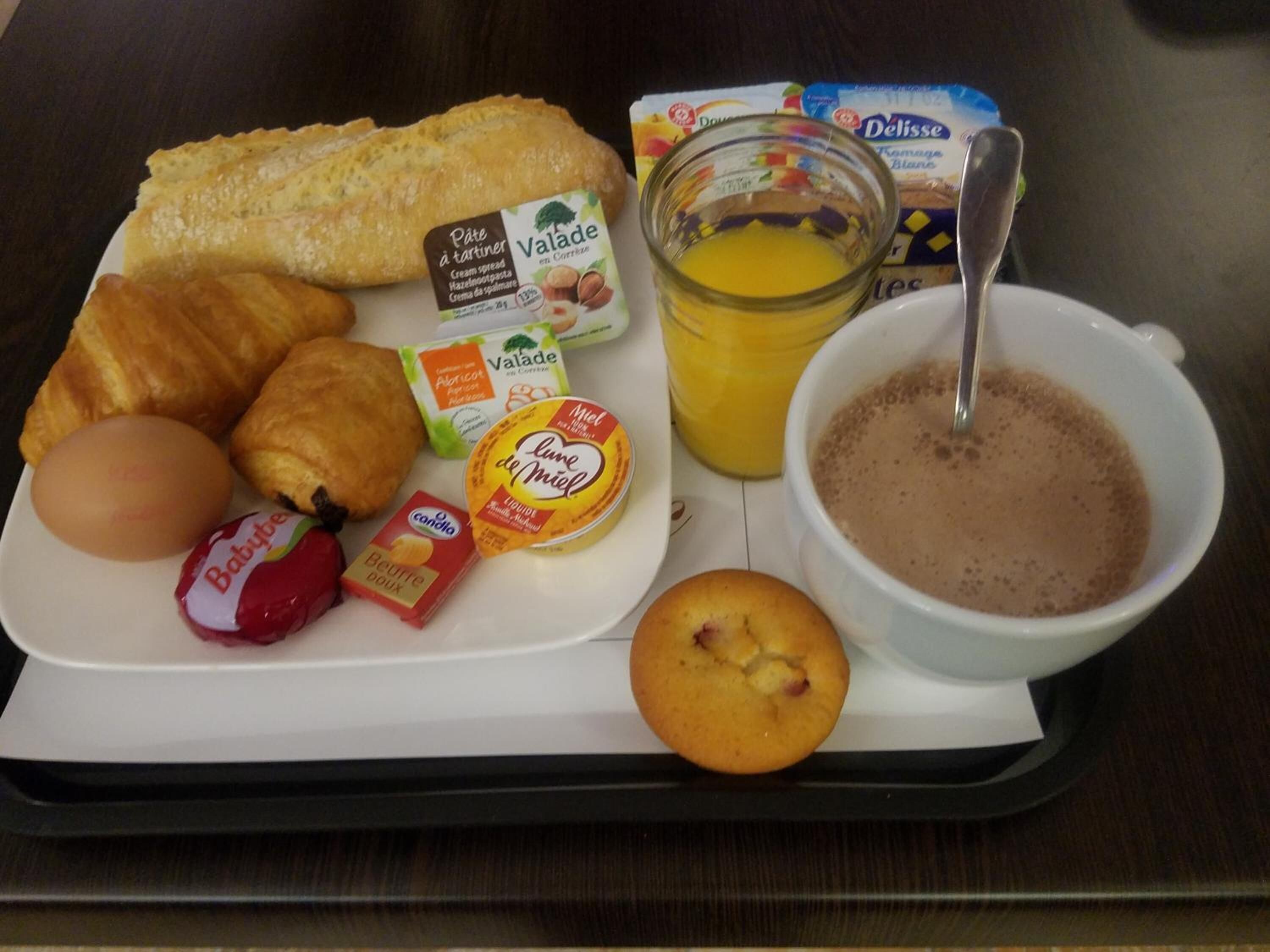 Bandeja con alimentos para desayuno, incluyendo croissants, huevos, un muffin, un tazón de café, un vaso de jugo de naranja y varias salsas y aderezos.
