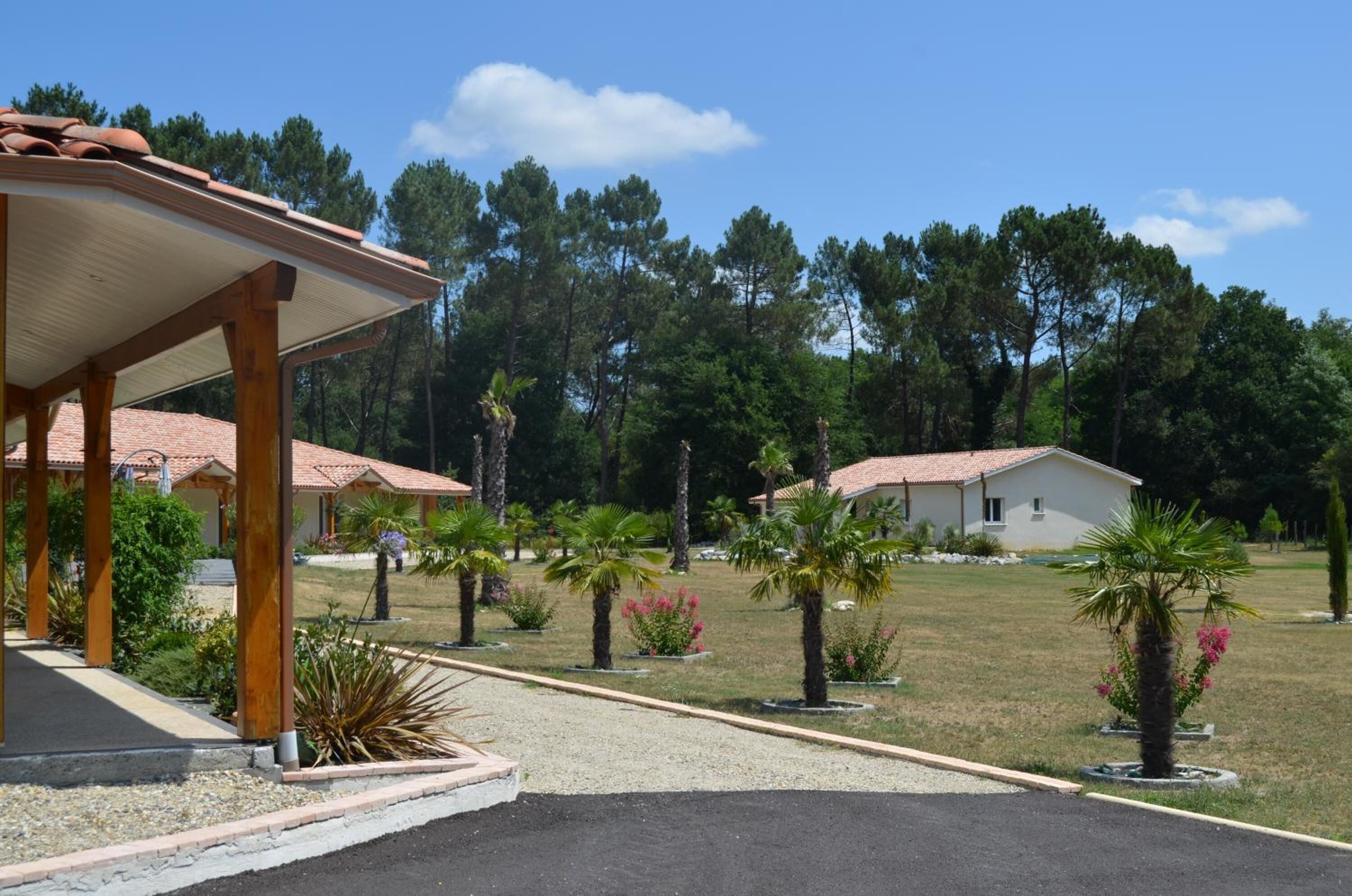 A resort with a covered pavilion, palm trees, and a grassy area with a building in the background.