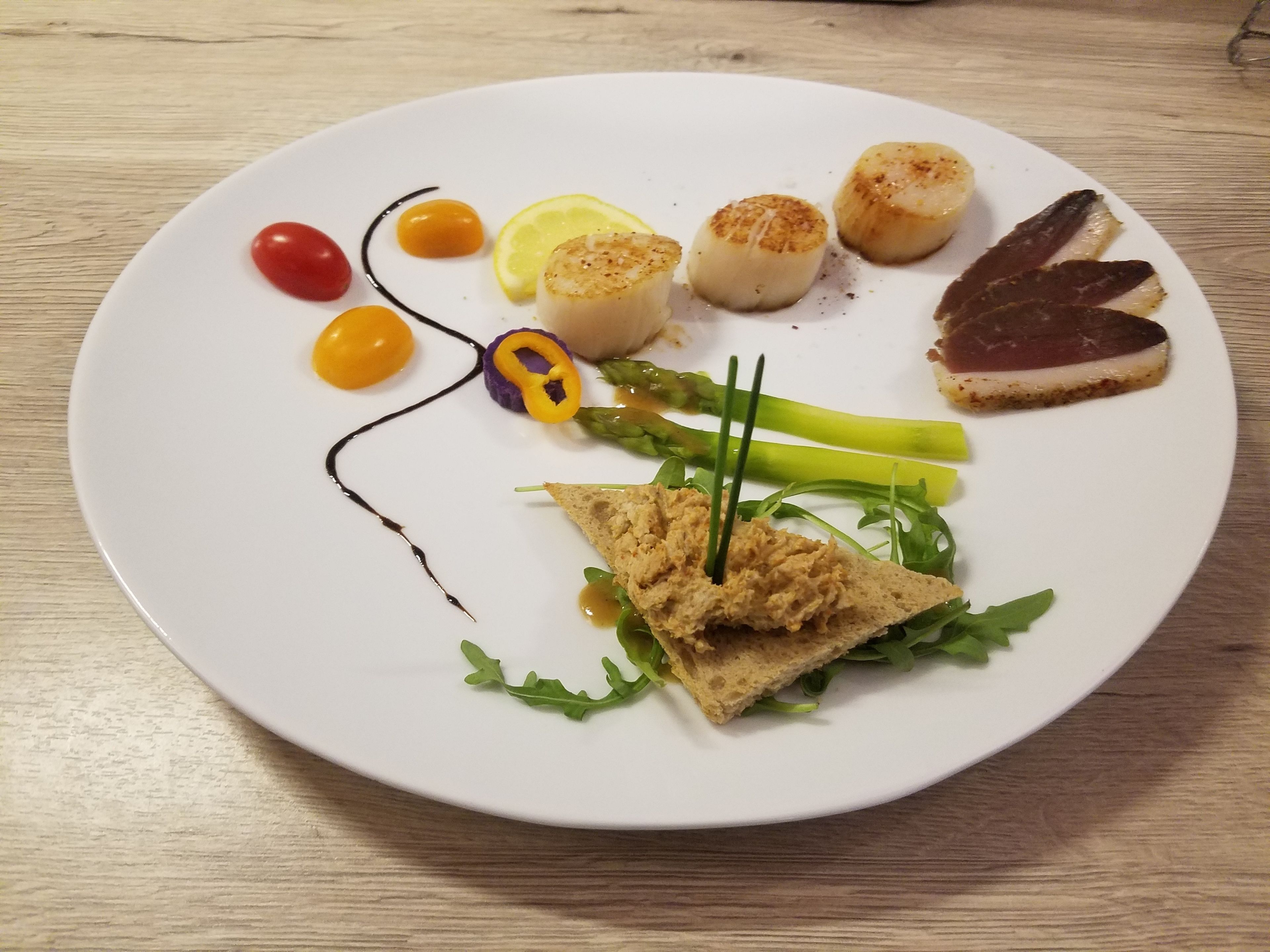 Un plato blanco con diversos alimentos, como vieiras, carne y verduras.